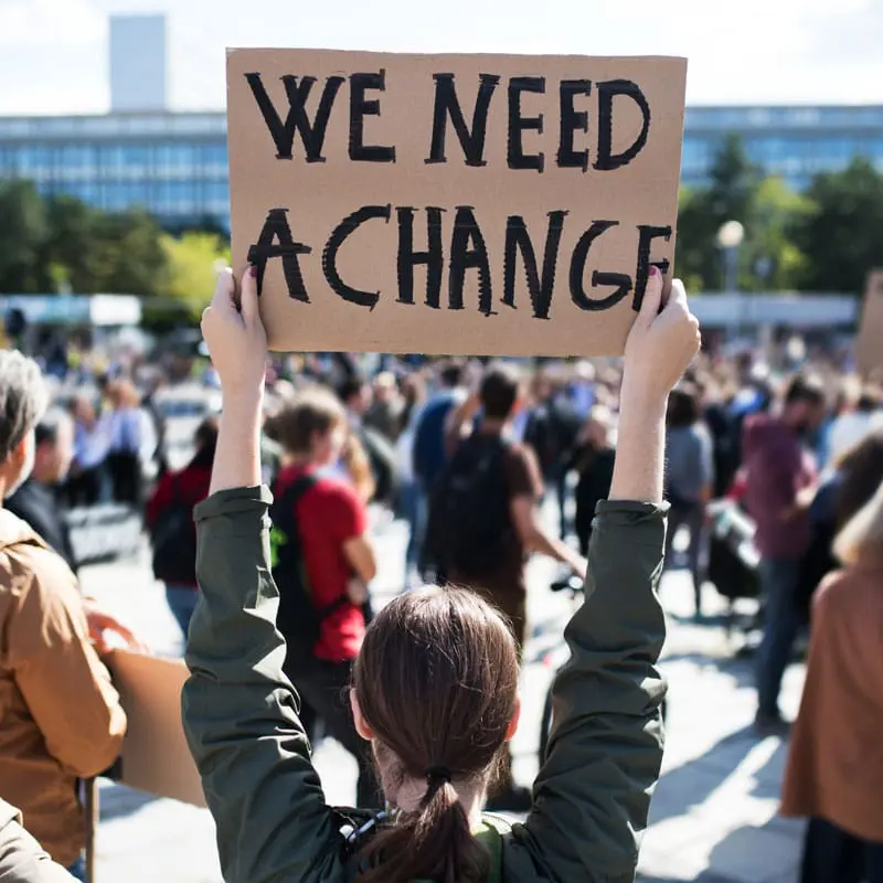 Woman holding up a cardboard sign saying we need a change like new AOT programs