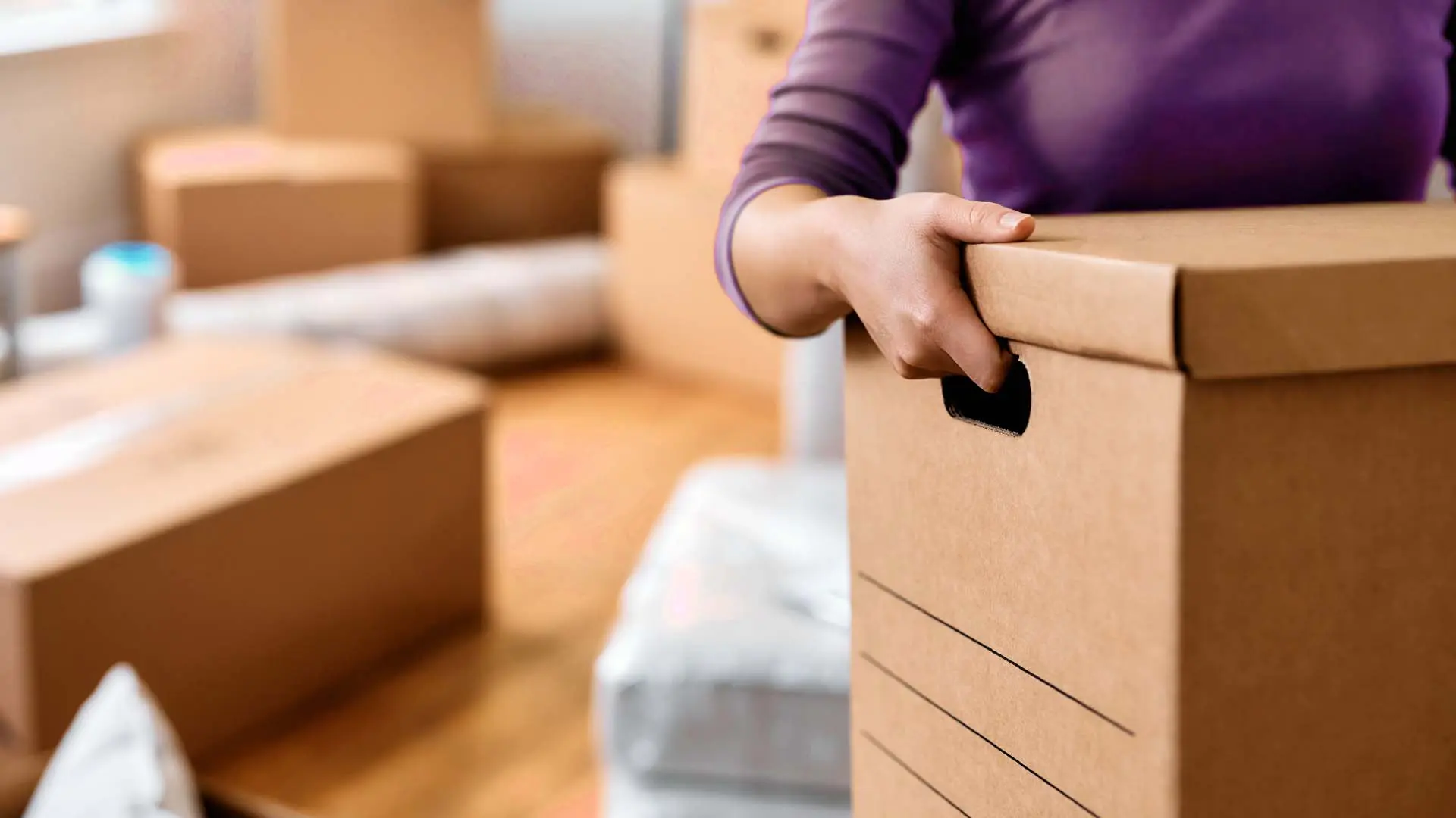A woman in a purple sweater moving boxes. In a new state she will seek severe mental illness resources for someone.