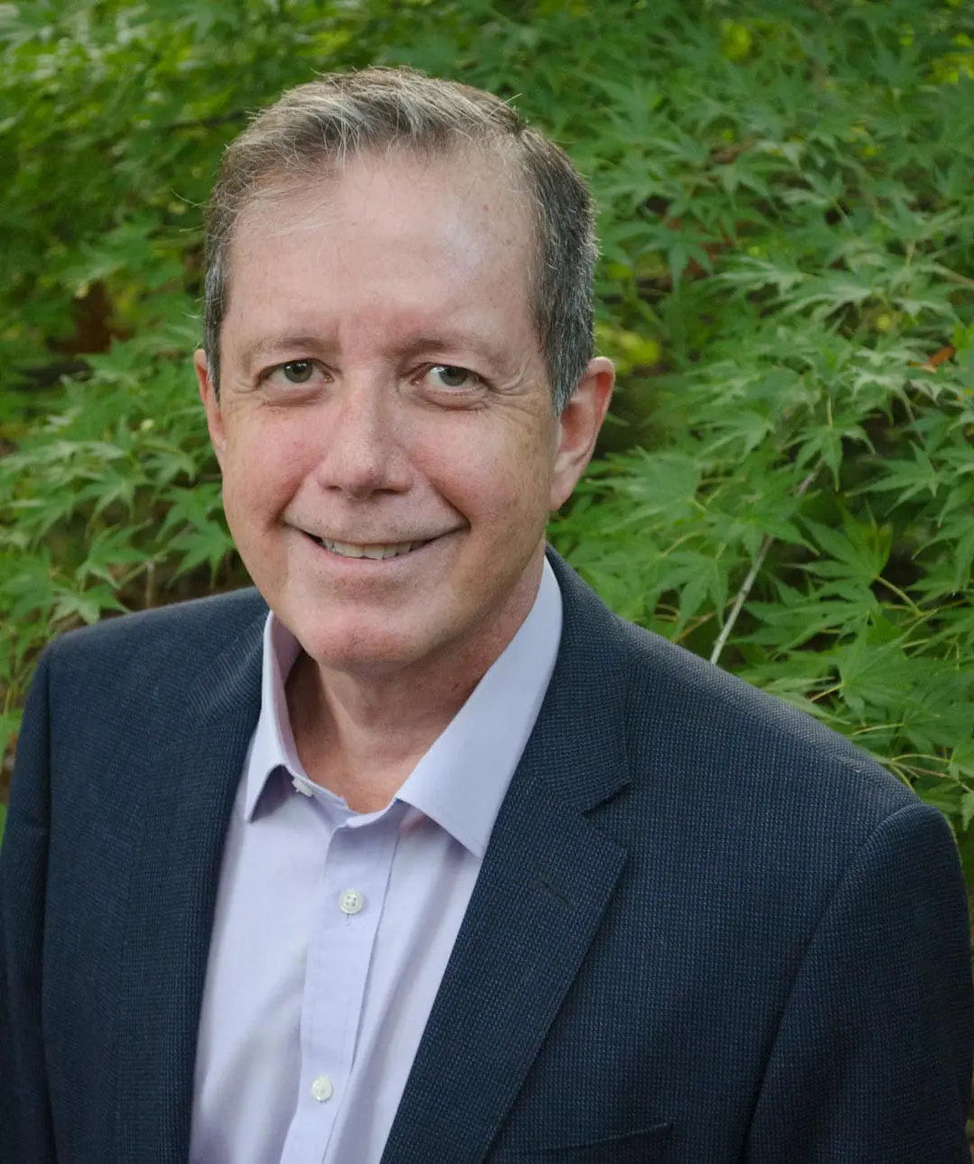 Dr. Xavier Amador in a suit, in front of a verdant green tree.