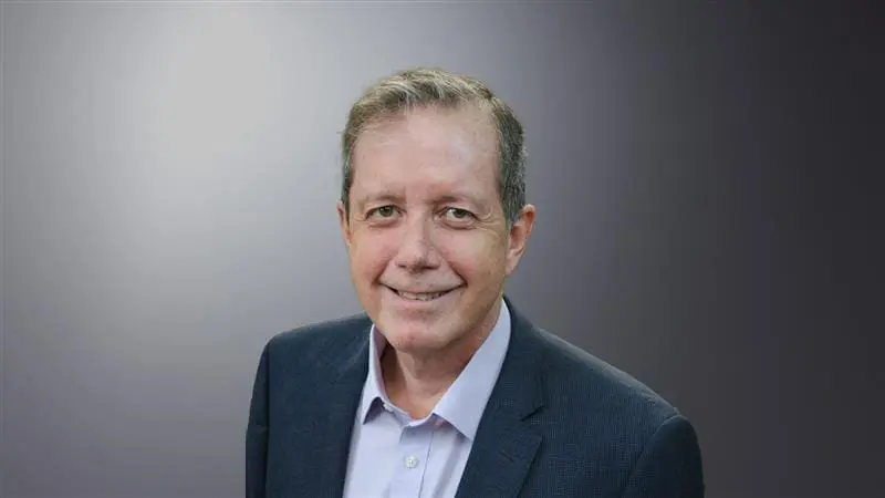 Dr. Xavier Amador, an older man with graying hair and a smile, in a suit and jacket, looking up at the camera against a gray background.