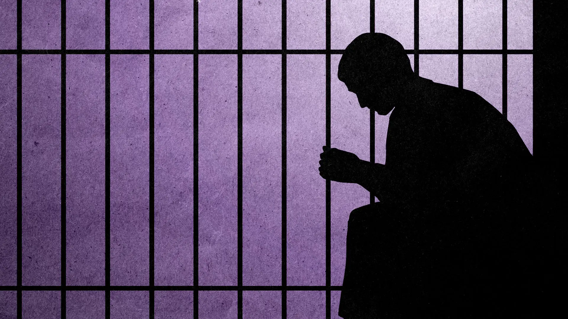 A silhouette of a person sitting down and leaning over against the backdrop of jail bars.