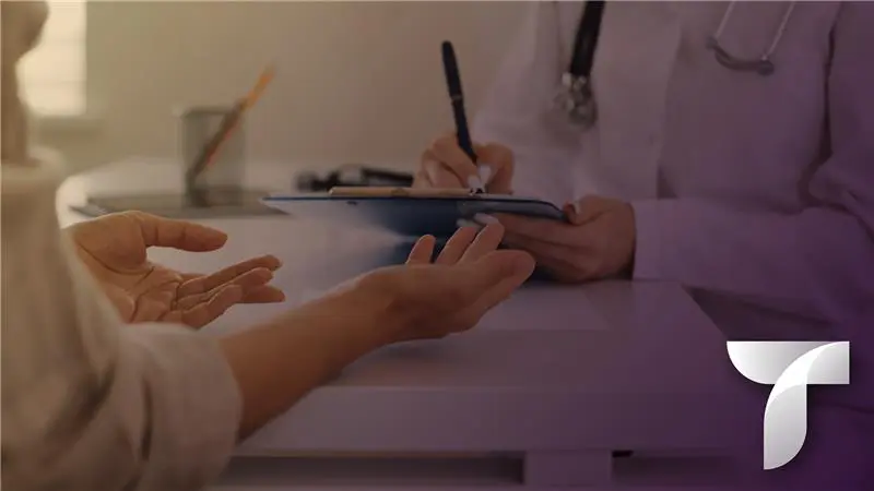 Close up picture of a doctor's hands writing on a clipboard, while a patient's hands gesture with open palms.